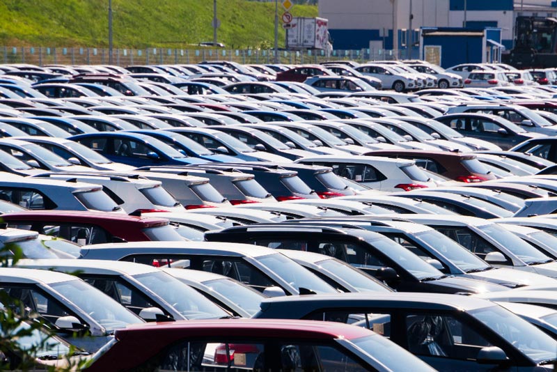 Ein dicht bepackter Parkplatz bei Gebrauchtwagen Ankauf Ratingen ist mit Reihen geparkter Autos in verschiedenen Farben, hauptsächlich Weiß und Rot, unter einem sonnigen blauen Himmel gefüllt.