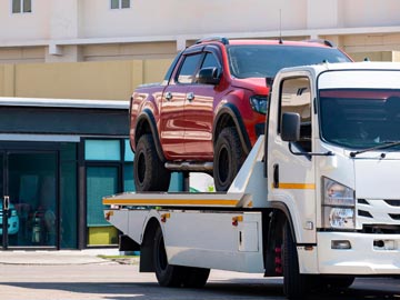 Ein rotes Pickup wird in einer sonnigen städtischen Umgebung auf einen weißen Abschleppwagen von Unfallwagenankauf Ratingen verladen.