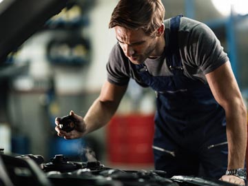 Ein Mechaniker in blauen Overalls inspiziert einen Motor und verwendet ein kleines Werkzeug, während Dampf von den Motorenteilen in einer Werkstatt aufsteigt.